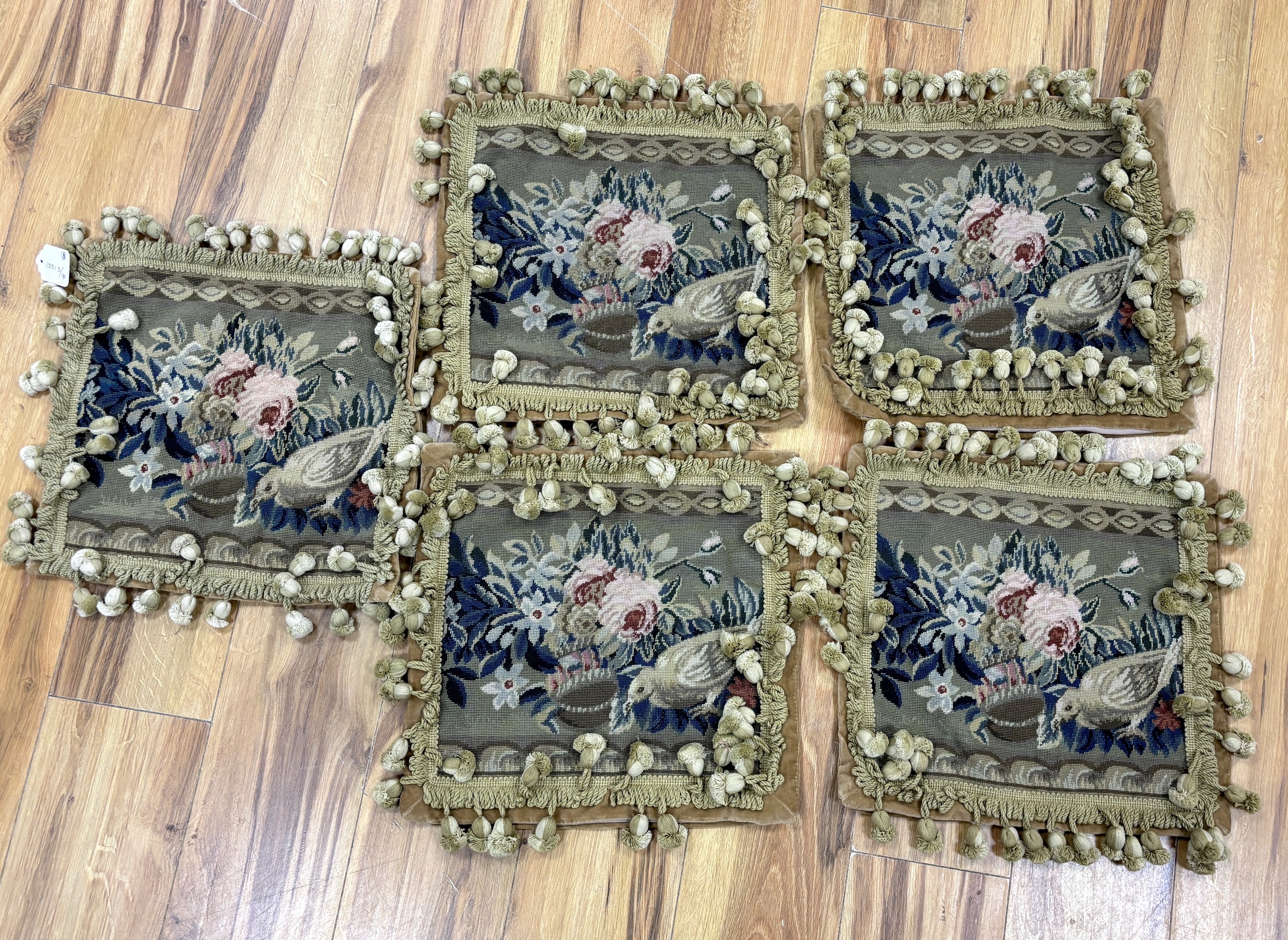 A set of five square woolwork cushion covers decorated with roses, and a bird, in greens, blues and pinks, edged with ornate tasseling and velvet backing, 37cm wide x 35cm high